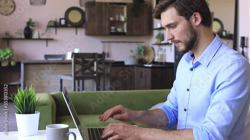 Side view happy young businessman is analizing financial documents from home during self isolation on laptop, sitting at table.