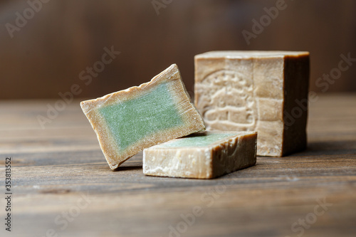 Bar and two slices of traditional aleppo organic laurel soap on a brown wooden background. photo