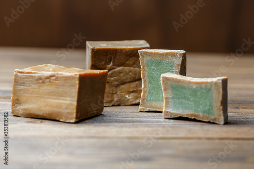 Fototapeta Naklejka Na Ścianę i Meble -  Two bars and slices of traditional aleppo organic laurel soap on a brown wooden background.
