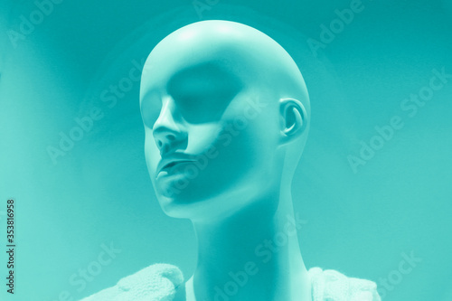 White plastic mannequin of a girl in a white sweater. Mannequin head behind glass on a clothing store window. Toned photo.