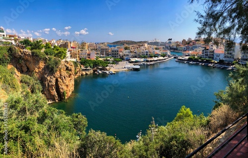 Agios Nikolaos Lake View Point. Lookout Point at Beautiful Lake with rocks, greenery and colorful city buildings.