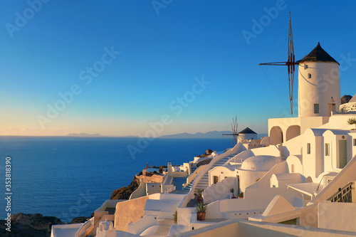 Traditional whitewashed windmills, hotels and apartments in Oia village, Santorini island, Greece on a sunset.
