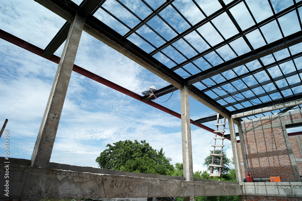 Worker doing the steelwork on the structure of metal roof by welding machine in the house under construction Worker doing the steelwork on the structure of metal roof by welding machine in the house under construction