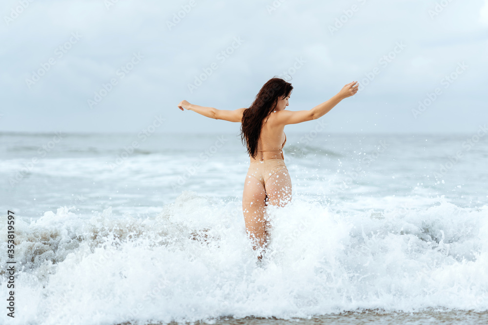 Outdoor summer fashion portrait of pretty sexy young woman in bikini posing behind blue ocean