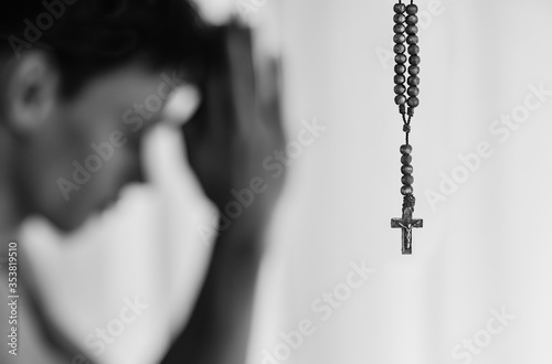 Vászonkép Black and white closeup of cross rosary with religious young man praying to god in the background