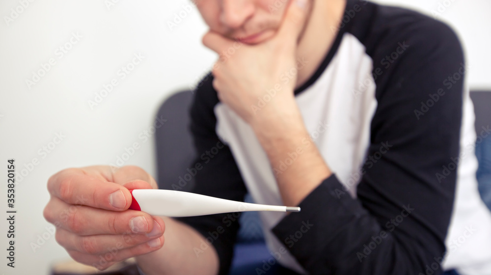 The man is checking his temperature lying in the bed looking on thermometer The man is checking his temperature lying in the bed looking on thermometer