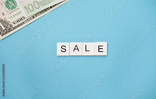 The Word Sale are spelled out in wooden letter tiles and banknotes on a blue trendy background. promotion seasonal offer ads.