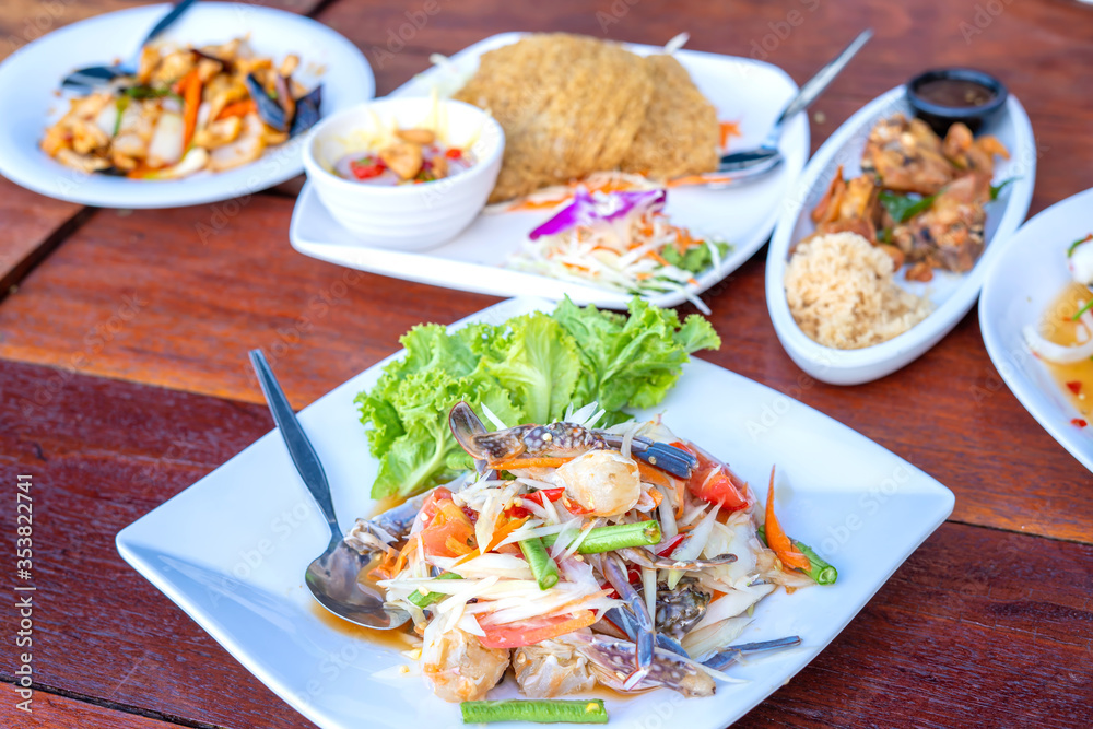 Papaya salad with fresh blue swimming crab, put papaya in a white dish and Thai food on a brown table in a restaurant Papaya salad with fresh blue swimming crab, put papaya in a white dish and Thai food on a brown table in a restaurant