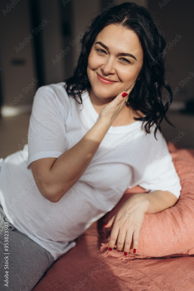 Close up portrait of a pregnant brunette woman looking to the camera. She is enjoying sunny morning in the bedroom. Woman feeling her future baby through the belly. Soft focus Close up portrait of a pregnant brunette woman looking to the camera. She is enjoying sunny morning in the bedroom. Woman feeling her future baby through the belly. Soft focus