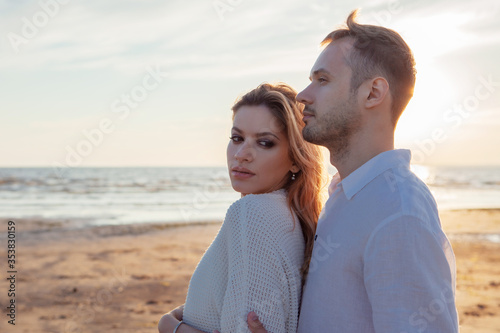 Love, romance, walk. Airy portrait of beautiful couple kissing on background of sunset sea, sandy beach and clouds.