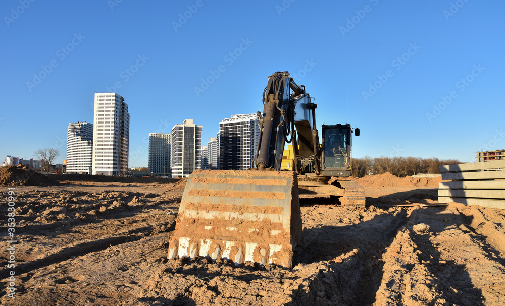 Excavators at earthworks on construction site. Backhoe loader digs a pit for the construction of the road. Digging trench for laying sewer pipes drainage in ground. Earth-Moving Heavy Equipment Excavators at earthworks on construction site. Backhoe loader digs a pit for the construction of the road. Digging trench for laying sewer pipes drainage in ground. Earth-Moving Heavy Equipment