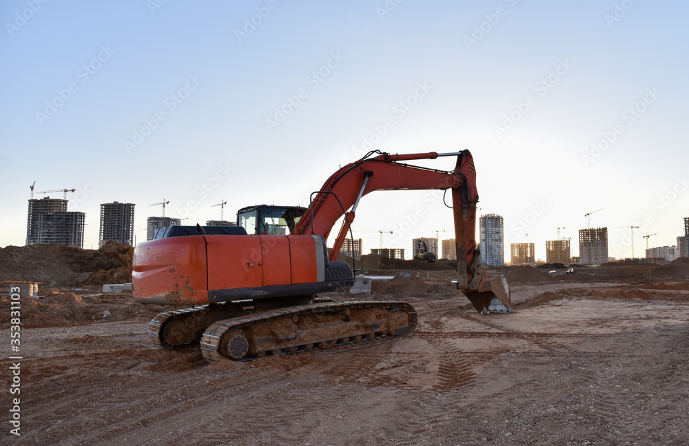 Excavator working at construction site on earthworks. Backhoe on road work digs ground. Paving out sewer line. Construction machinery for excavating, loading, lifting and hauling of cargo Excavator working at construction site on earthworks. Backhoe on road work digs ground. Paving out sewer line. Construction machinery for excavating, loading, lifting and hauling of cargo