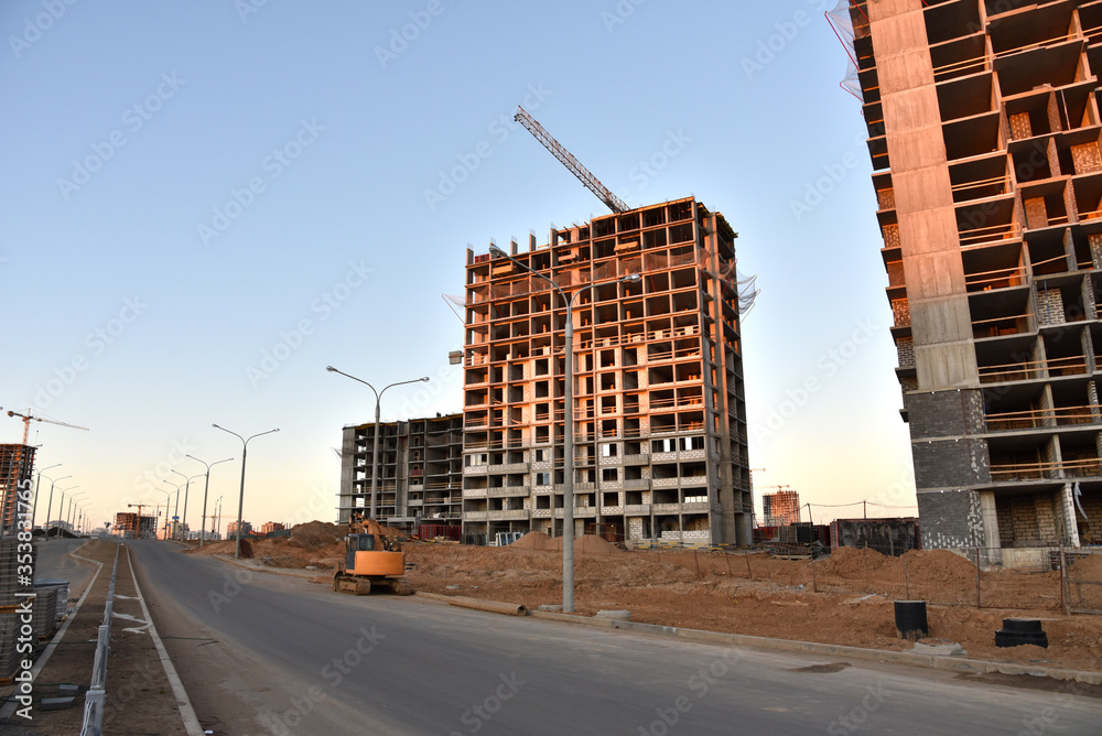 View on the large construction site with tower cranes and buildings on sunset background. Multi-storey residential building is being constructed use of crane. Concept of renovation program
