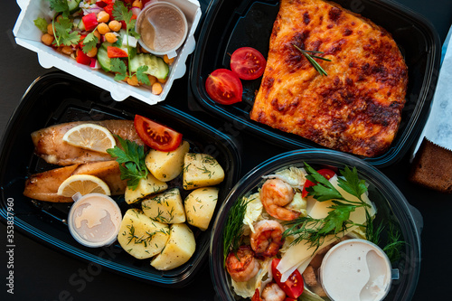 Delivery service food in plastic lunch boxes on a black background. Low key, healthy food, colorful flat lay. Food concept.