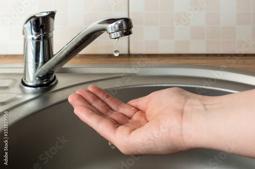 A drop of water from faucet drips in woman palm above round metal kitchen sink