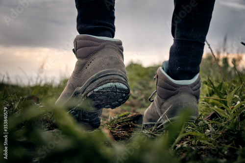 rear view of female hiking boots on green grass with sky background. Trekking and outdoor concept.