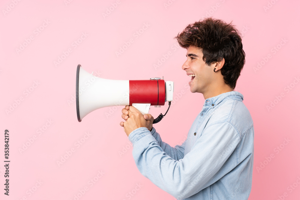 Young caucasian man with jean shirt over isolated pink background shouting through a megaphone Young caucasian man with jean shirt over isolated pink background shouting through a megaphone