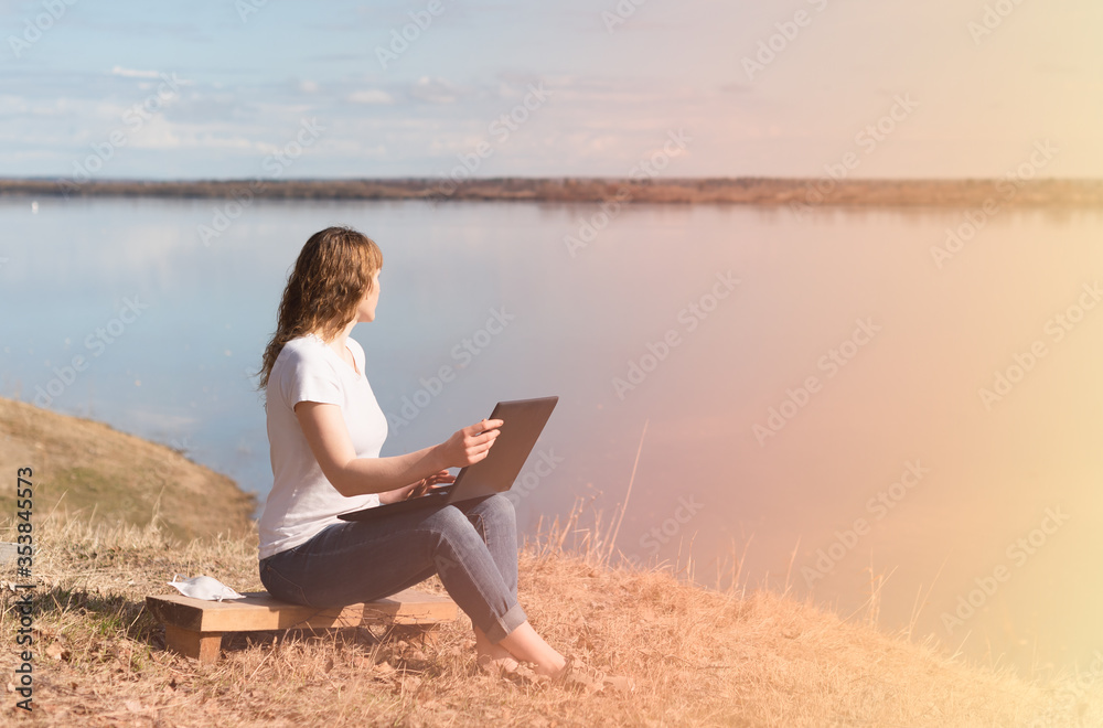 woman working remotely on a laptop outdoors, on a background of river and sky