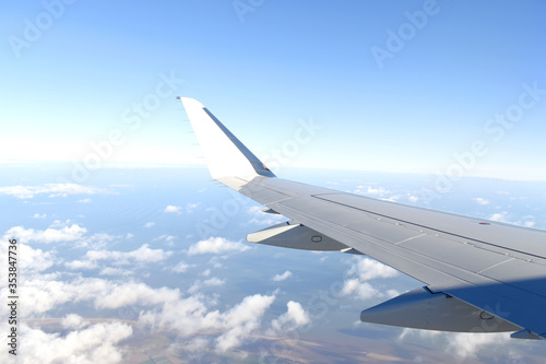 Airplane wing flying above clouds in blue sky, view from airplane window