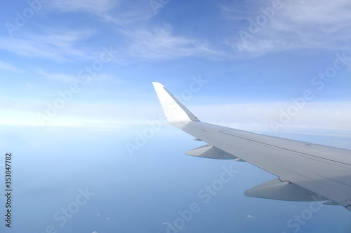 Airplane wing flying above clouds in blue sky, view from airplane window