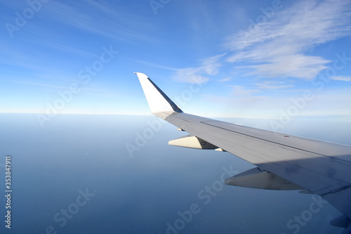 White wing of airplane fiying above clouds with horizon blue sky