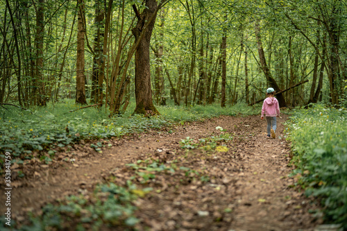 little child girl in dense forest walks along trail into depths forest.