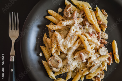 penne pasta and boscaiola topping sauce in a dish with fork closeup - top view photo