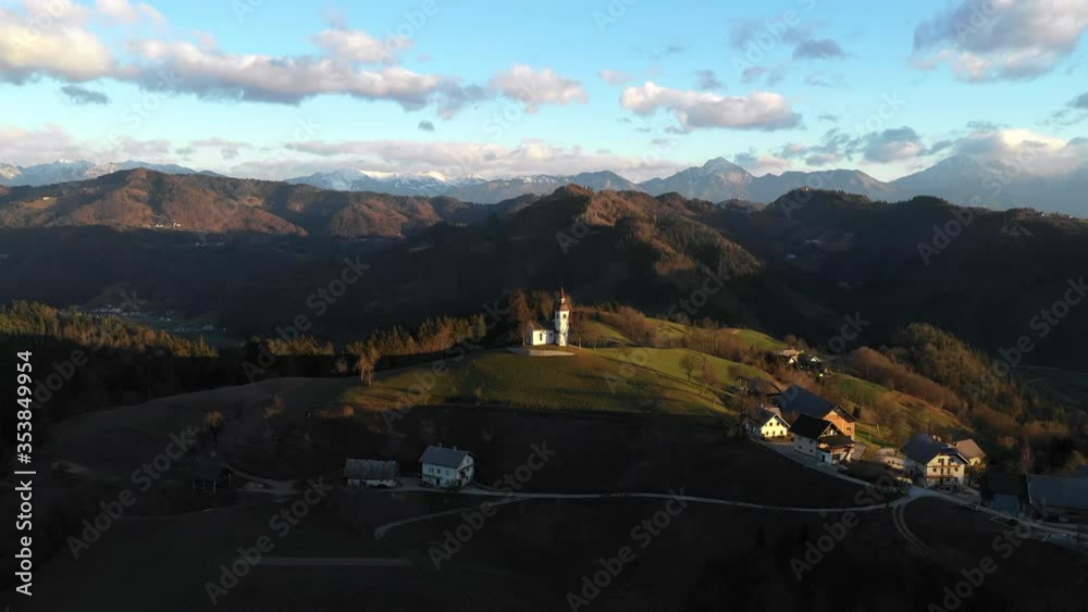 Aerial shot of church on mountain in town during sunrise, drone flying forward over landscape against sky - Bled, Slovenia Aerial shot of church on mountain in town during sunrise, drone flying forward over landscape against sky - Bled, Slovenia