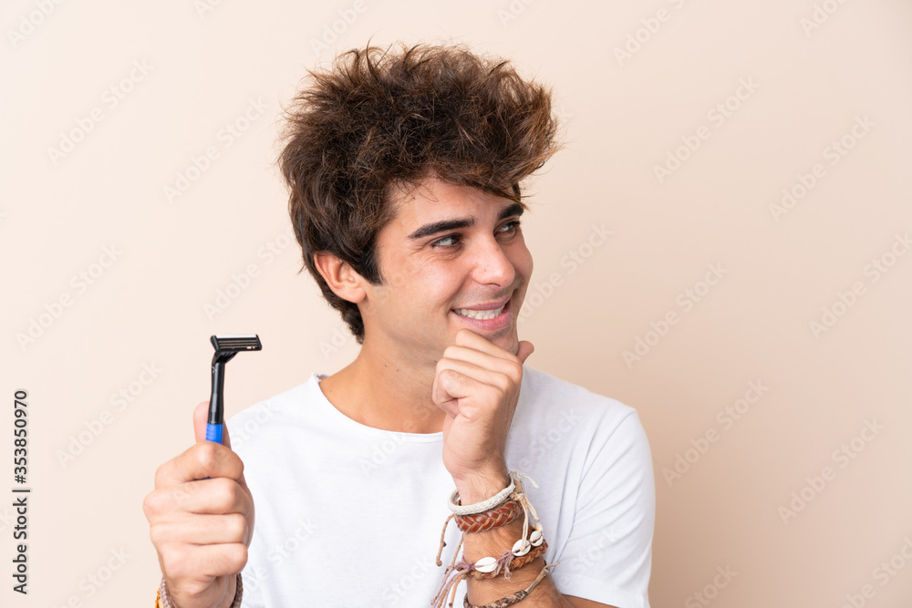 Young handsome man shaving his beard thinking an idea and looking side Young handsome man shaving his beard thinking an idea and looking side