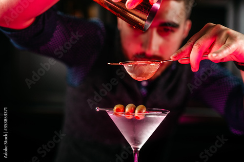 Photos Professional bartender pouring and preparing martini with olives at bar counter
