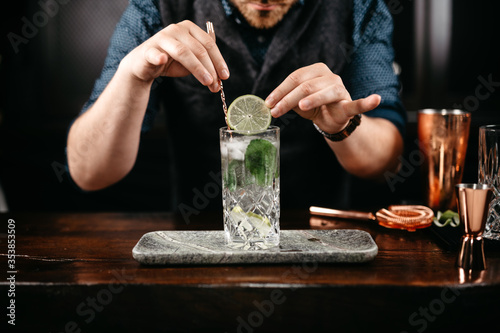 Professional bartender pouring and preparing gin and tonic with lime at bar counter. Details of mixology photo