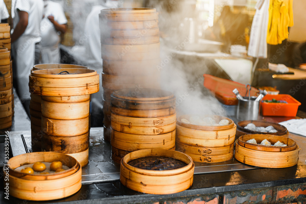 Piles of stacking bamboo steamers are steaming for dim sum in front of the restaurant with blur chefs in background in Taipei, Taiwan. Focus on front bamboo steamers. Piles of stacking bamboo steamers are steaming for dim sum in front of the restaurant with blur chefs in background in Taipei, Taiwan. Focus on front bamboo steamers.