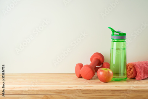 Fitness and healthy lifestyle background with bottle of water, dumbbells and apple on wooden table