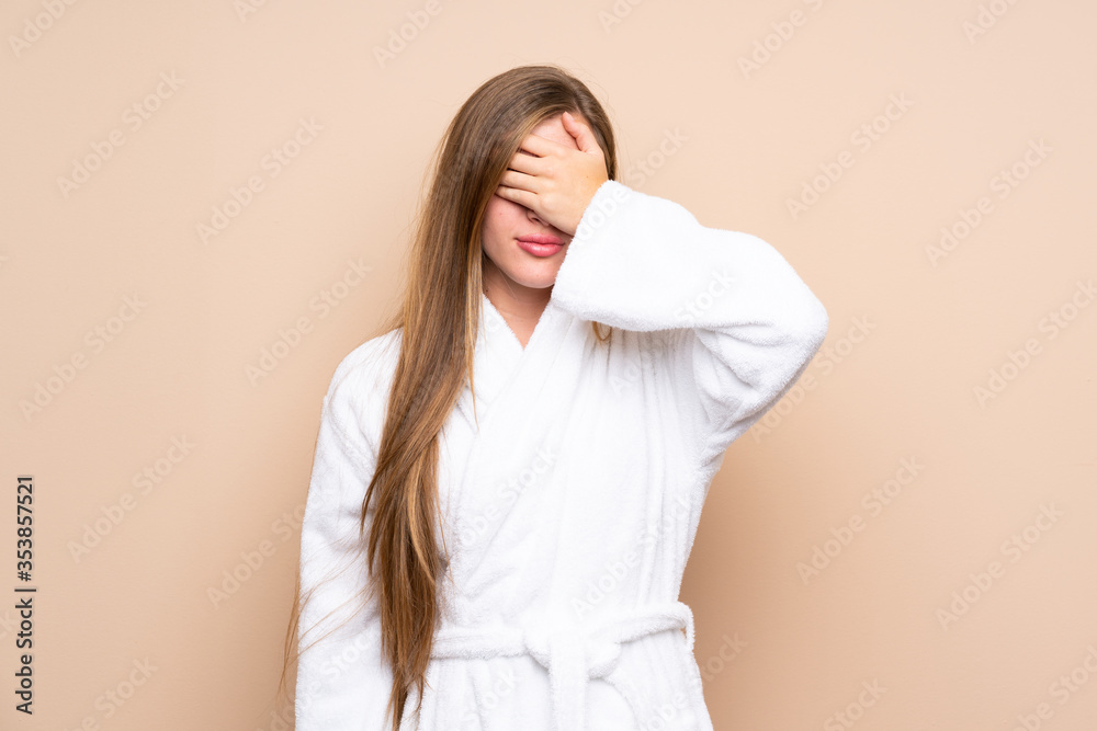 Teenager girl in a bathrobe over isolated background covering eyes by hands Teenager girl in a bathrobe over isolated background covering eyes by hands