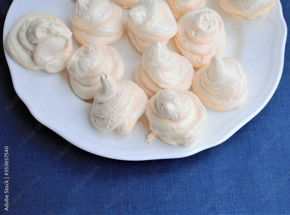 Homemade french white meringues on a round plate, on a background of texture of blue linen cloth Homemade french white meringues on a round plate, on a background of texture of blue linen cloth