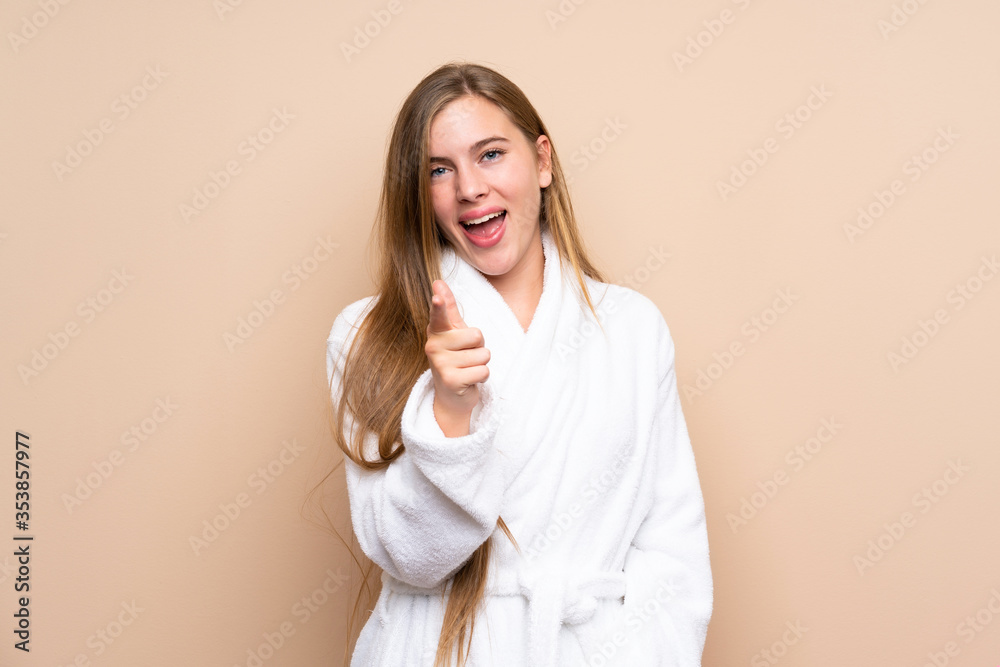 Teenager girl in a bathrobe over isolated background points finger at you Teenager girl in a bathrobe over isolated background points finger at you