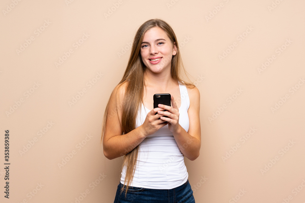 Teenager blonde girl over isolated background sending a message with the mobile Teenager blonde girl over isolated background sending a message with the mobile