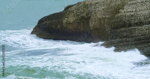 Slow motion shot of waves splashing to the rocks on a cloudy day. 