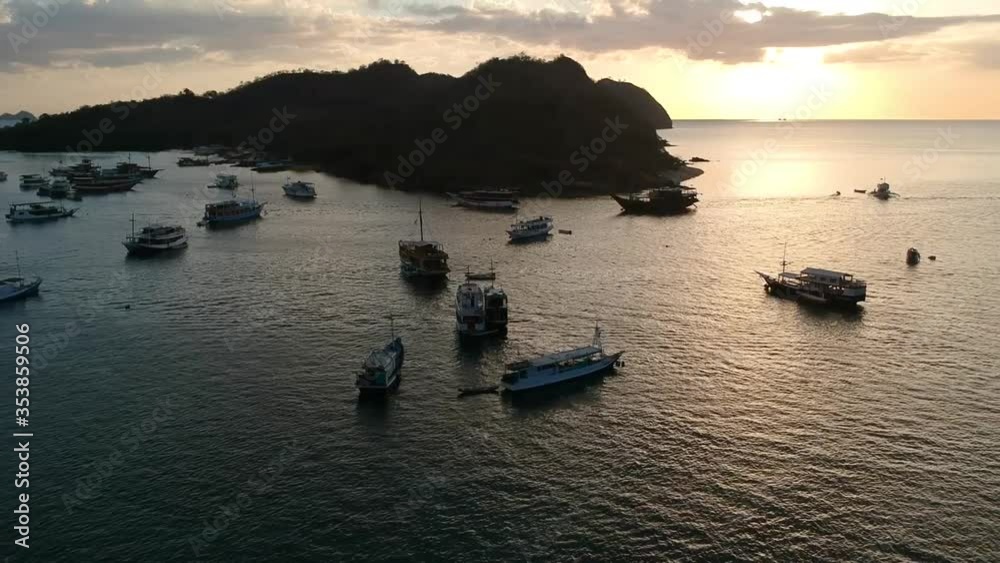 Aerial Drone, sunset/sunrise clip of boats floating on water in busy harbor, calm ocean, islands in background, Indonesia Aerial Drone, sunset/sunrise clip of boats floating on water in busy harbor, calm ocean, islands in background, Indonesia