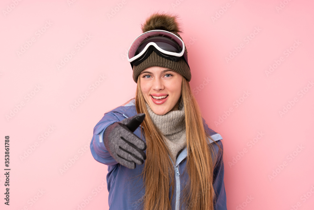 Skier teenager girl with snowboarding glasses over isolated pink background handshaking after good deal