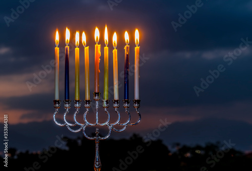 Menorah with light of candles is traditional symbol for Hanukkah Holiday, blurred sky and clouds background, selective focus on burning candles
