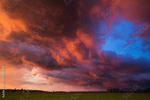 Landscape with majestic colorful dramatic red sky with fluffy clouds at sunset before before a thunderstorm and rain with the spacious field.