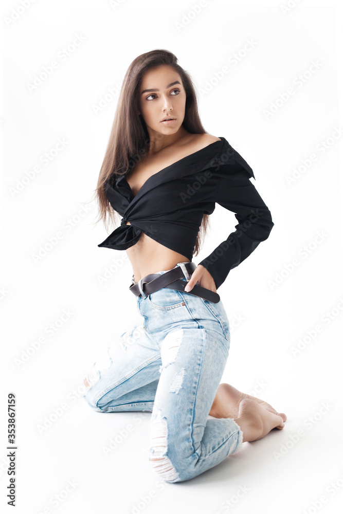 Young cool hipster girl in black shirt and blue banana jeans kneeling on white background