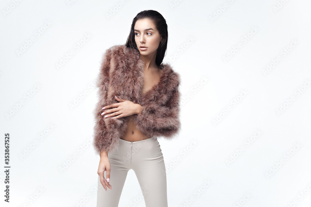 Young elegant girl posing in fluffy pink cape with artificial fur and beige flare trousers on gray background Young elegant girl posing in fluffy pink cape with artificial fur and beige flare trousers on gray background