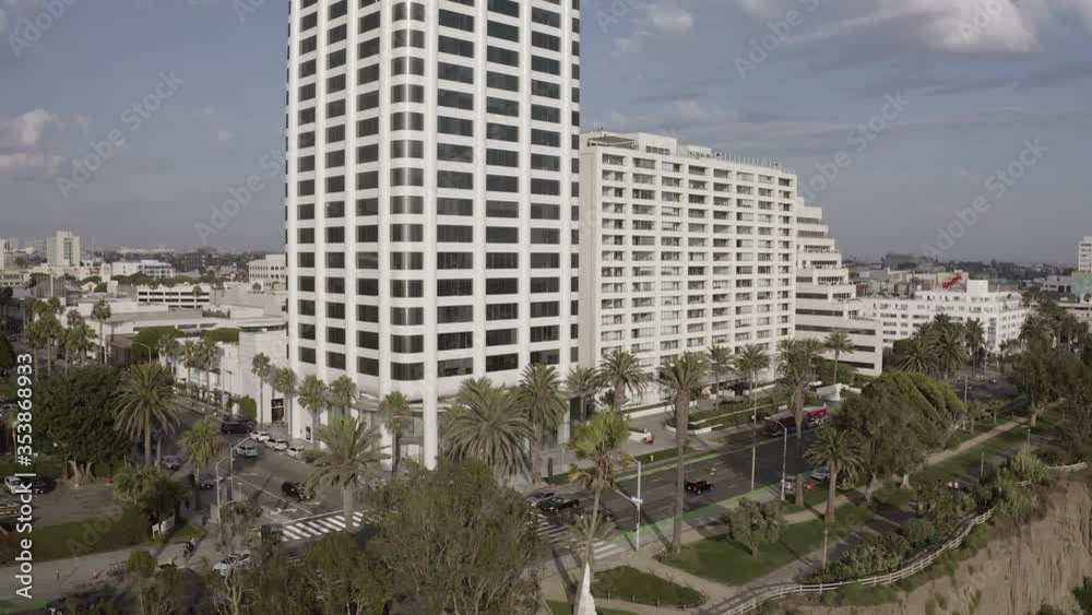 Aerial shot of vehicles on street by trees and buildings in city, drone descending over cliff against sky on sunny day - Santa Monica, California Aerial shot of vehicles on street by trees and buildings in city, drone descending over cliff against sky on sunny day - Santa Monica, California
