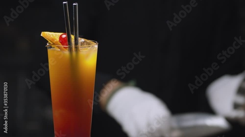 Close up tequila sunrise cocktail slowly rotating on the table. Barmans hands playing shaker on background. Beautiful shot of long drink. Bar drinks series.