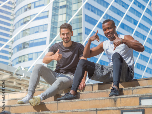 Two diverse athletes showing positive thumbs up while sitting or resting after exercising.