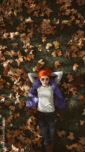 flat lay de mujer de pelo naranja tumbada boca arriba sobre hojas de otoño