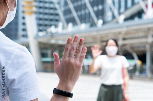 asian woman wearing face mask standing apart on the sky walk in city and say hi to each other as a social distancing guideline during covid-19 or coronavirus outbreak. new normal lifestye concept photo