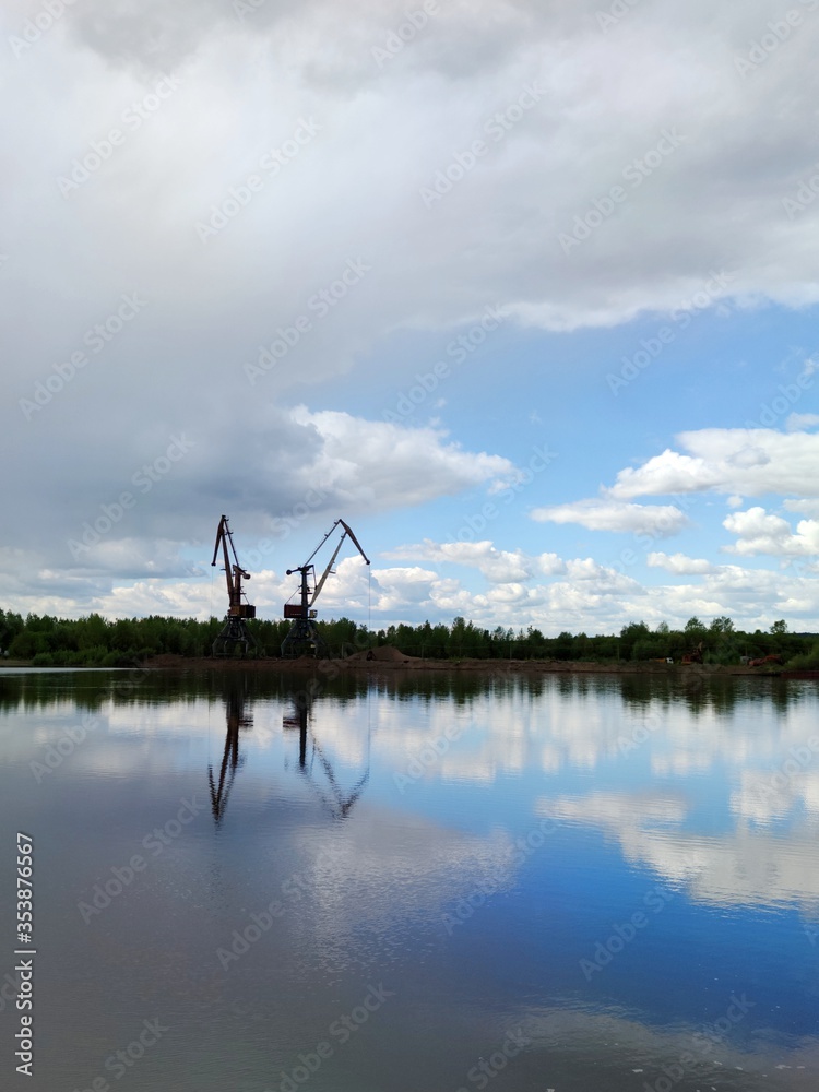 two cranes on the river bank against a beautiful sky with clouds reflected on the surface of the water